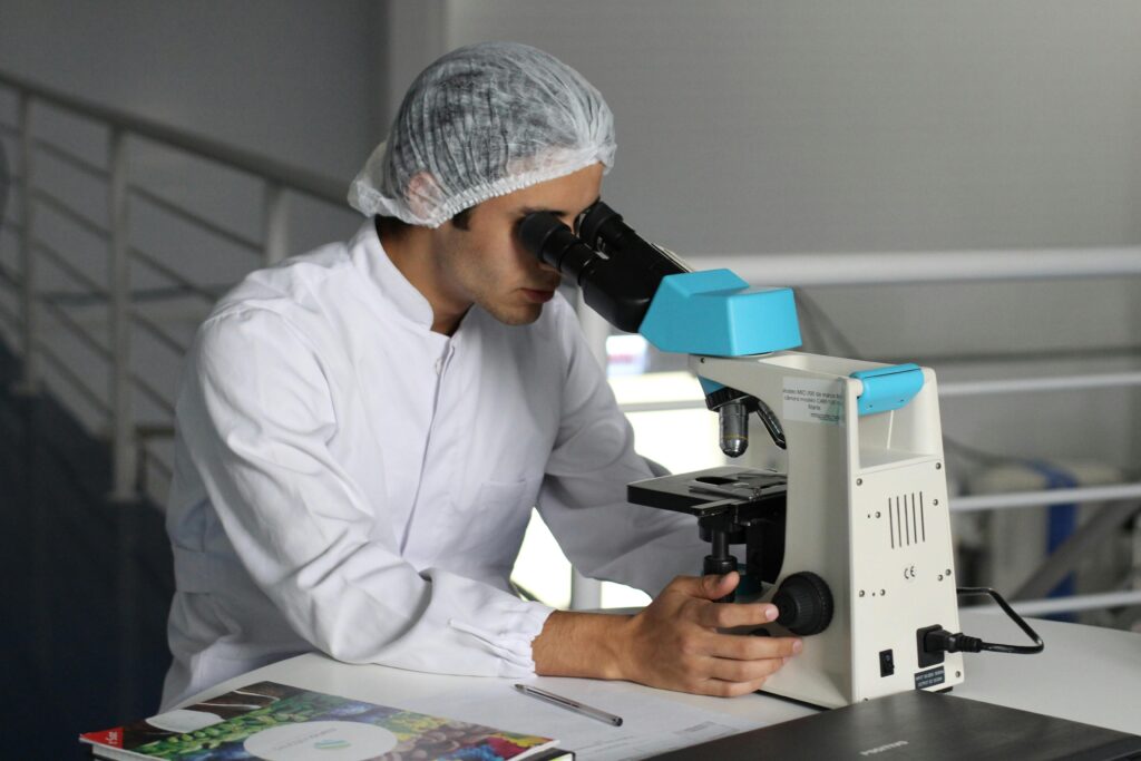 Scientist in a lab coat using a microscope to conduct research, focusing on healthcare improvements.